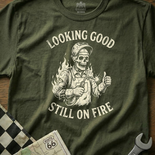 Olive green t-shirt with skeleton welder giving thumbs up, text "Looking good, still on fire."