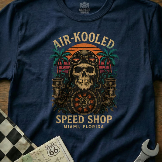 Skull wearing goggles, holding motorcycle wheel, with palm trees and sunset.