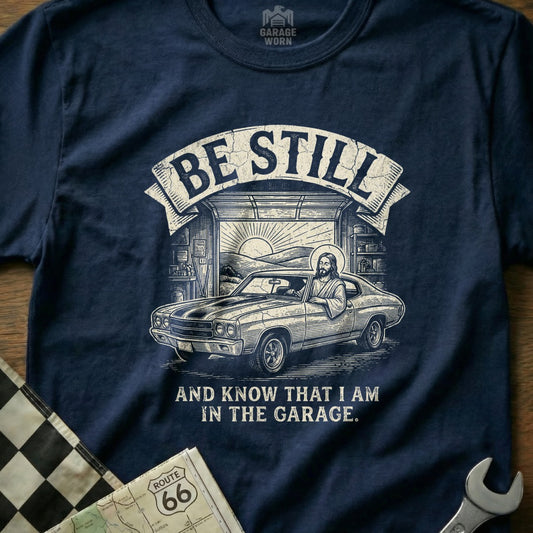 Jesus driving a classic car in a garage, with "Be Still and Know That I Am In The Garage" text.