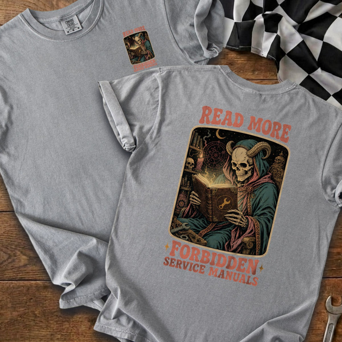 Grey t-shirt with graphic of skeleton reading a book titled "Read More Forbidden Service Manuals".