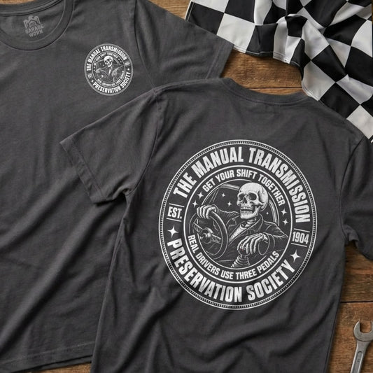 Dark gray t-shirt with a circular graphic featuring a skeleton driving, labeled "The Manual Transmission Preservation Society."