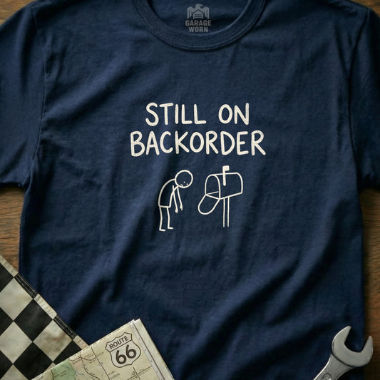 Navy t-shirt with "Still on Backorder" text and stick figure by mailbox.