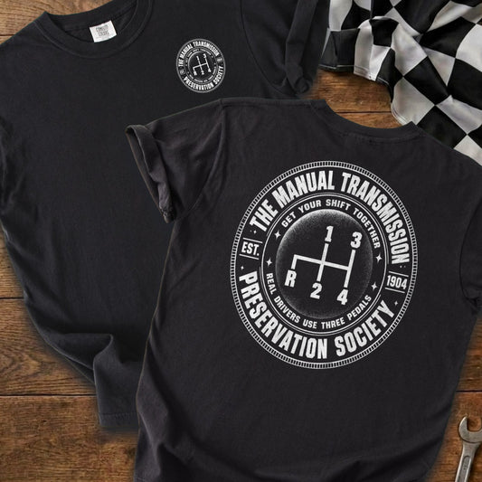 Black t-shirt with circular manual transmission shift pattern graphic and text.