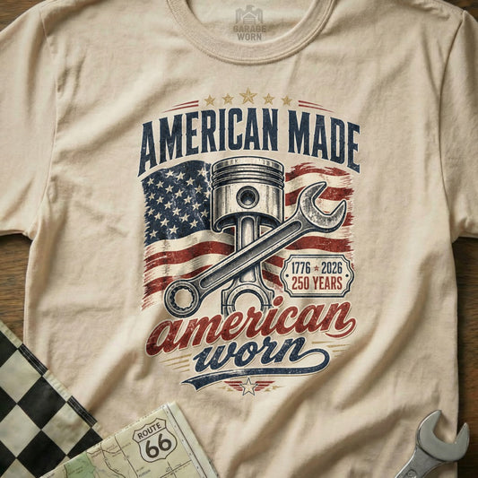 Cream t-shirt with "American Made American Worn" text, piston, wrench, and US flag graphic.