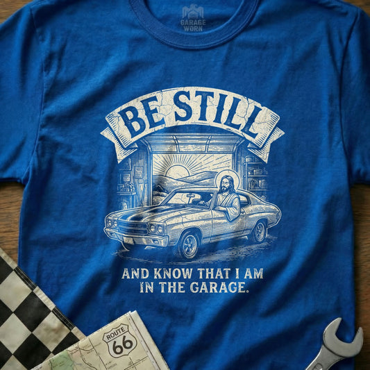T-shirt with Jesus driving a classic car in a garage, reading "Be Still and Know That I Am In The Garage."