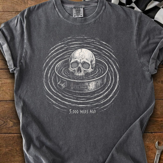 T-shirt graphic: skull in an oil drain with concentric circles and text "3,000 MILES AGO".