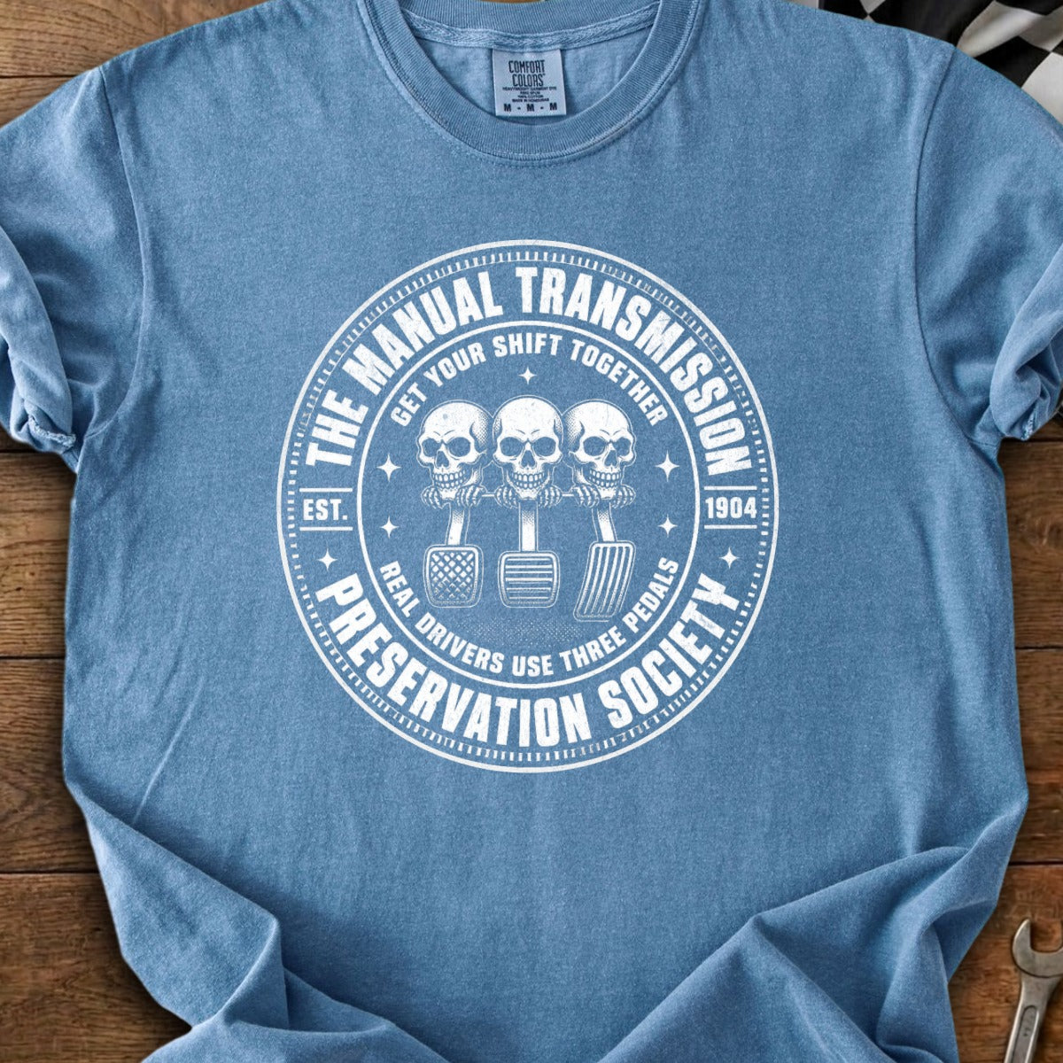 Manual transmission preservation society design with skulls and three pedals.