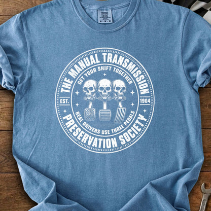 Manual transmission preservation society design with skulls and three pedals.