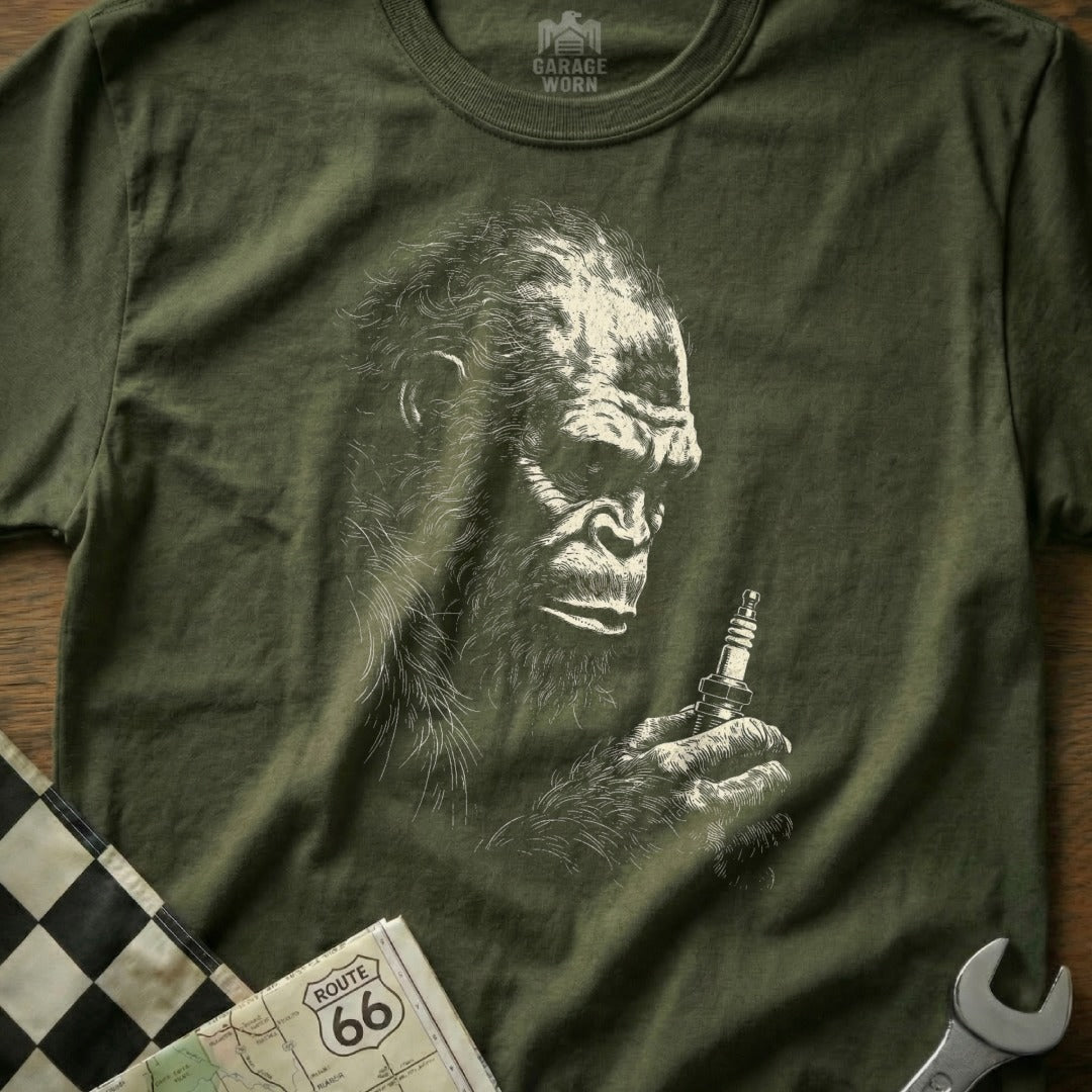 Olive green t-shirt with Bigfoot holding a spark plug.