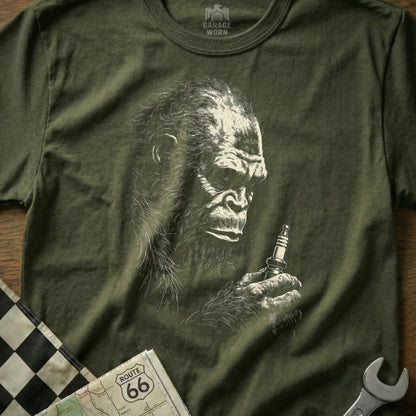 Olive green t-shirt with Bigfoot holding a spark plug.