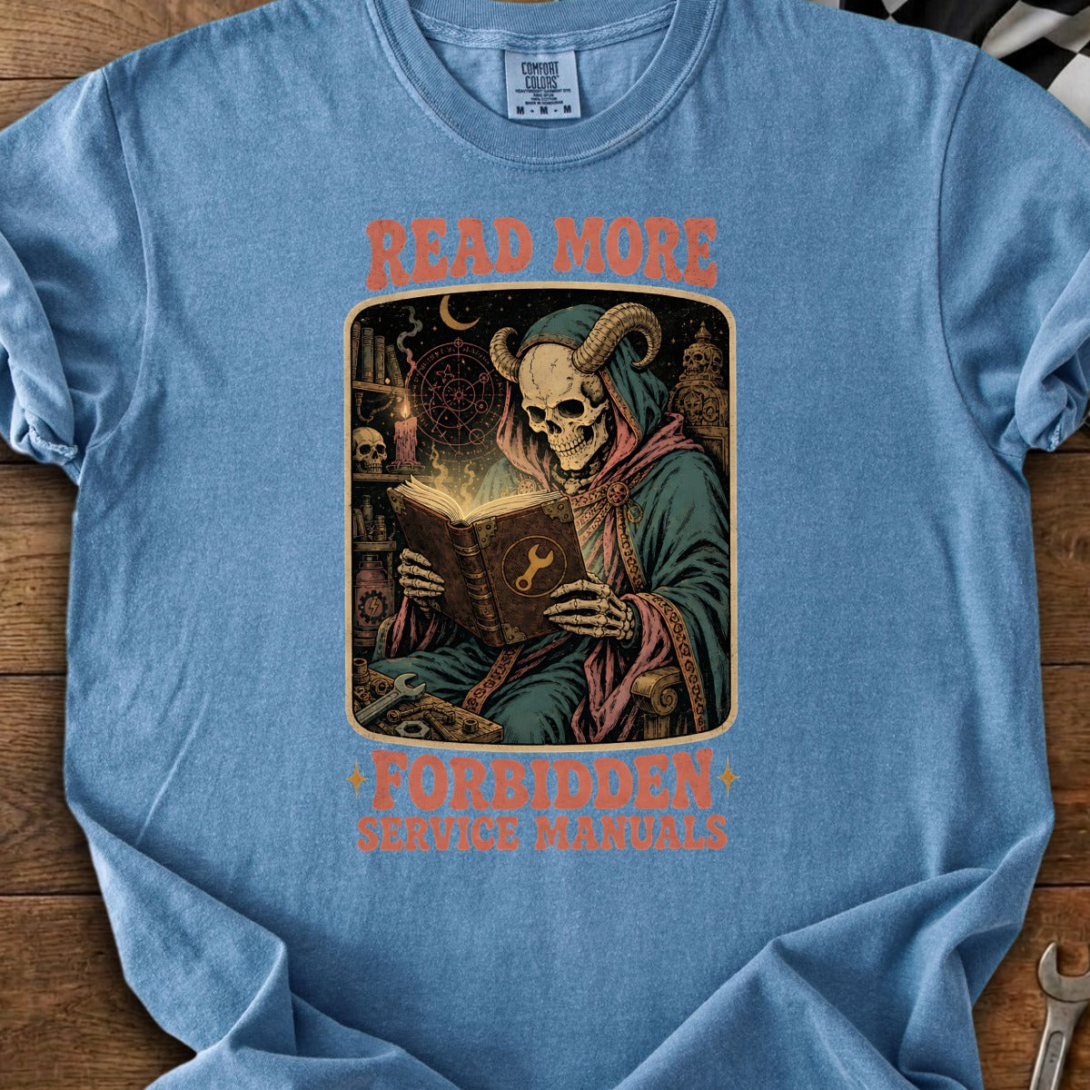 T-shirt with a horned skeleton reading a book titled "Forbidden Service Manuals" with "Read More" text.
