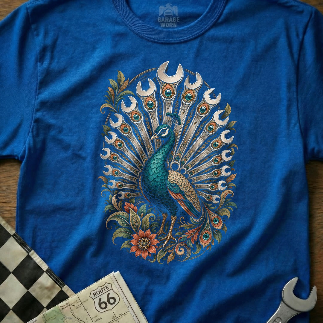 Blue t-shirt with a peacock design featuring wrenches as feathers and floral accents.