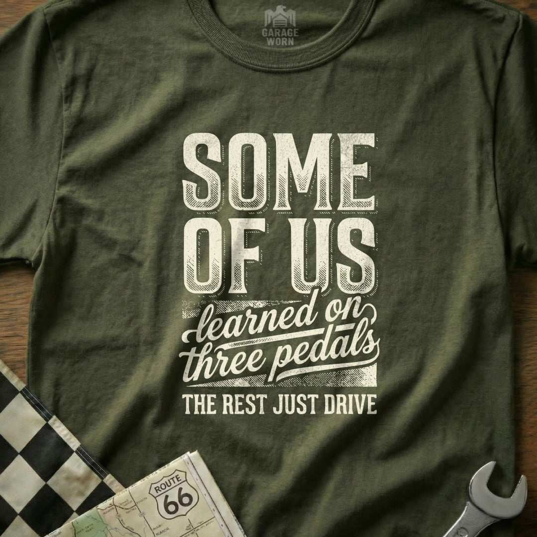 Olive green t-shirt with "SOME OF US learned on three pedals THE REST JUST DRIVE" text.