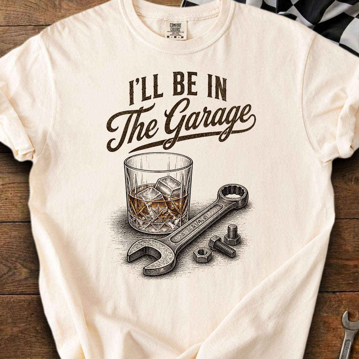 Cream t-shirt with "I'll Be In The Garage" text above a glass of whiskey and tools.