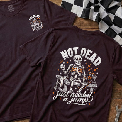 Dark t-shirt with skeleton getting a jump start, "NOT DEAD just needed a jump."