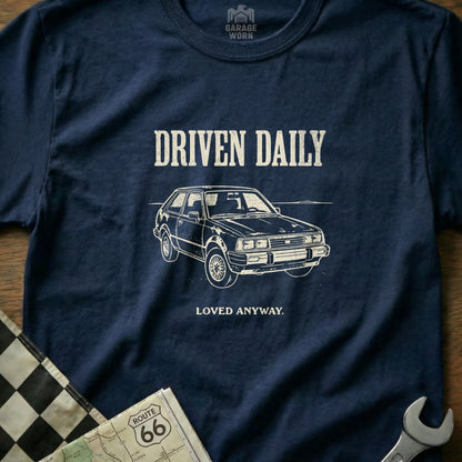 T-shirt with "DRIVEN DAILY LOVED ANYWAY" text and drawing of a classic car.
