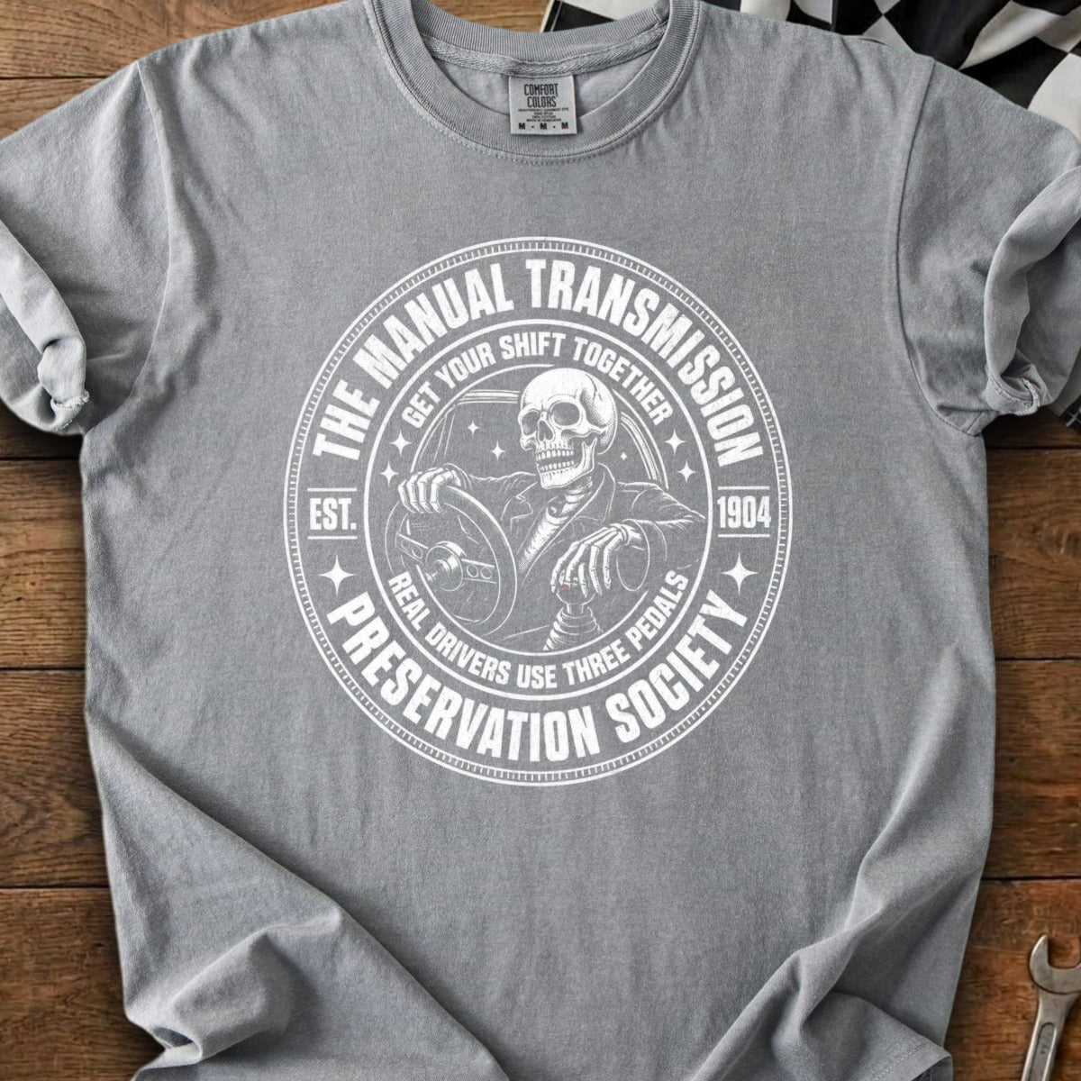 T-shirt with white graphic of skeleton driving, "The Manual Transmission Preservation Society" text.