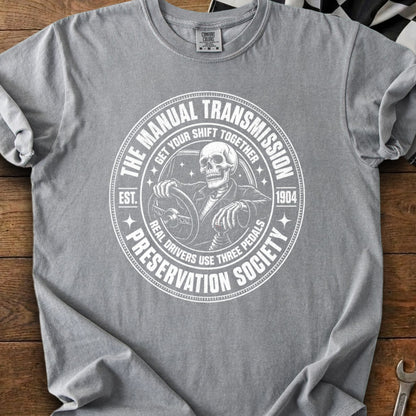 T-shirt with white graphic of skeleton driving, "The Manual Transmission Preservation Society" text.