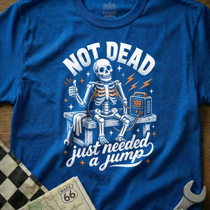 Skeleton with jumper cables and charger on a bench, text "NOT DEAD just needed a jump".