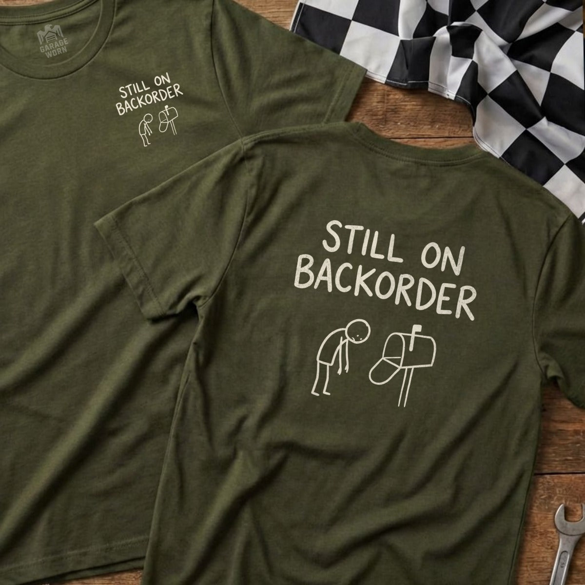 Green t-shirt with "Still on Backorder" text and stick figures by a mailbox.