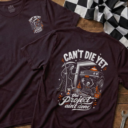 T-shirt with Grim Reaper, skeleton, and car graphic, reads "Can't Die Yet, The Project Ain't Done."