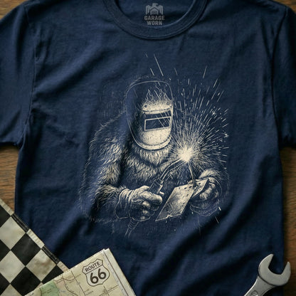 T-shirt graphic of a Bigfoot character welding with sparks flying.