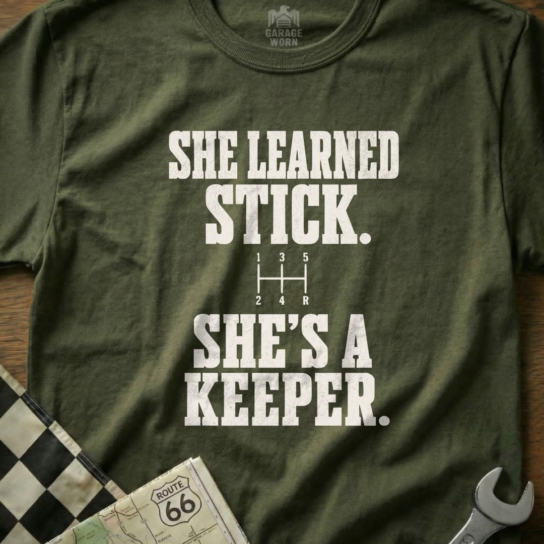 Olive green t-shirt with "SHE LEARNED STICK. SHE'S A KEEPER." text.