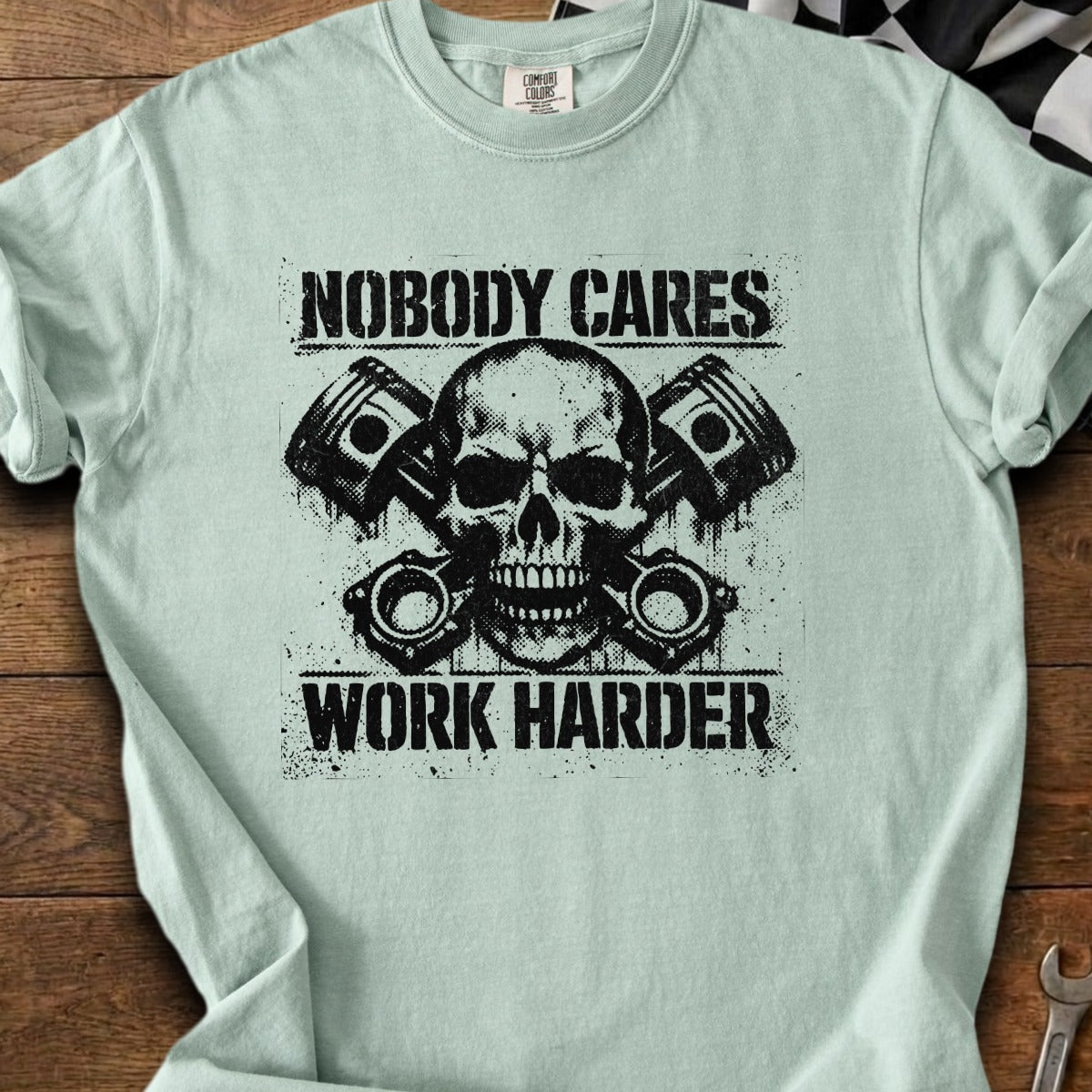 Light blue t-shirt with a distressed skull, pistons, and text reading "NOBODY CARES WORK HARDER".
