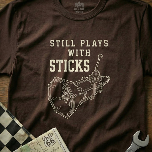 Brown t-shirt with "Still Plays with Sticks" and manual transmission diagram.