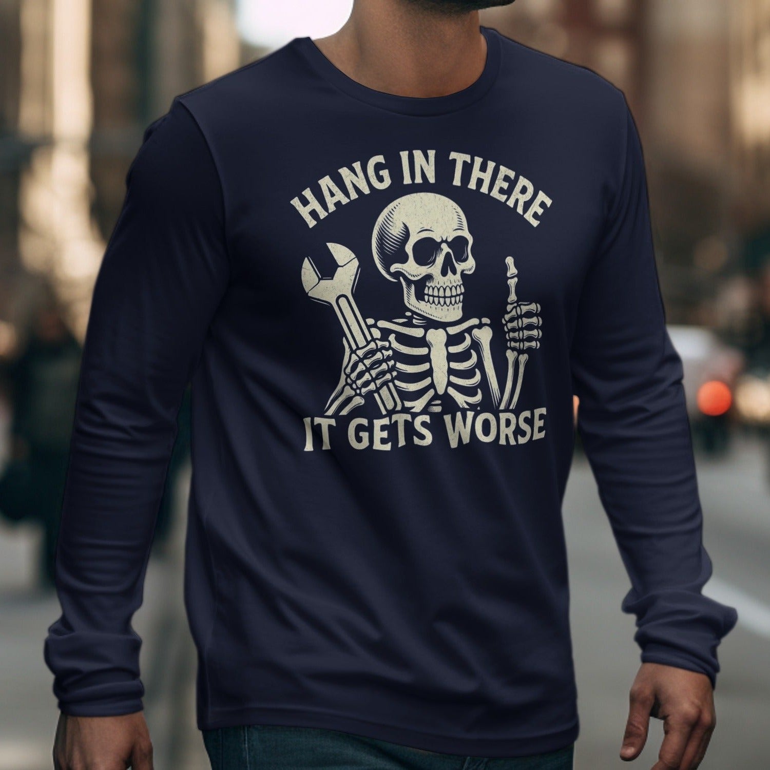 Skeleton with wrench and thumb up on dark blue long sleeve shirt, text reads "Hang In There It Gets Worse".