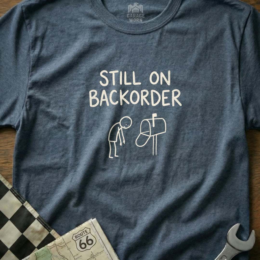 T-shirt with "Still on Backorder" text and graphic of a person and mailbox.