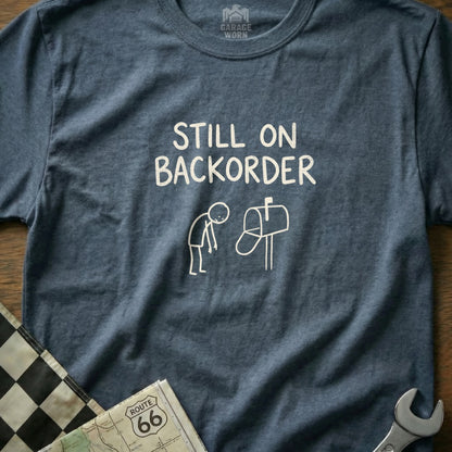 T-shirt with "Still on Backorder" text and graphic of a person and mailbox.