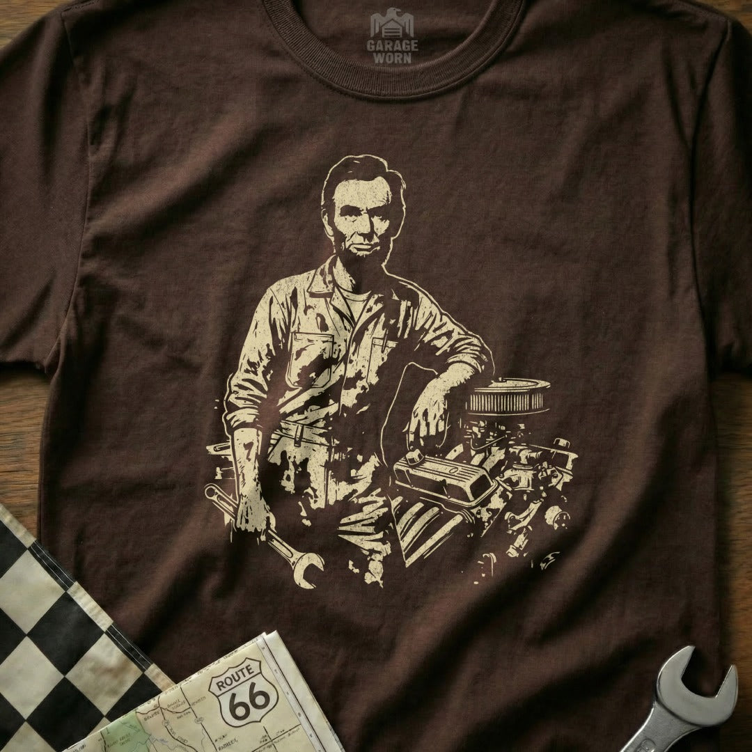 Abraham Lincoln graphic on brown t-shirt leaning on engine parts.