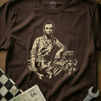 Abraham Lincoln graphic on brown t-shirt leaning on engine parts.
