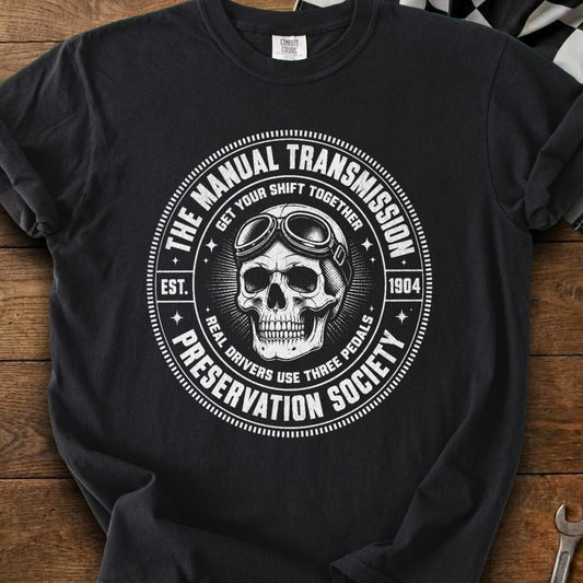 Black t-shirt with skull wearing goggles and manual transmission society logo.