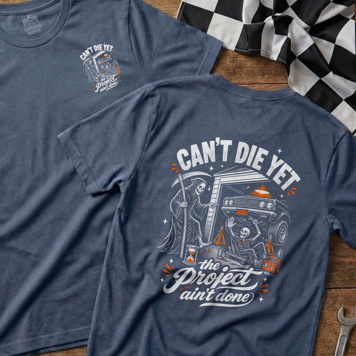 Blue t-shirt with Grim Reaper and skeleton working on car, text "Can't Die Yet, The Project Ain't Done".