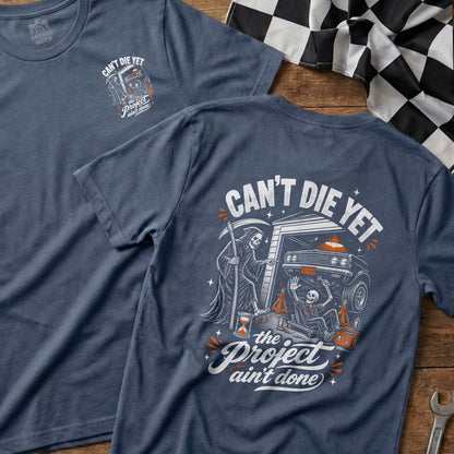 Blue t-shirt with Grim Reaper and skeleton working on car, text "Can't Die Yet, The Project Ain't Done".