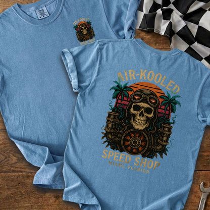 Light blue t-shirt featuring a skull with goggles, pistons, and palm trees; "AIR-KOOLED SPEED SHOP MIAMI FLORIDA" text.