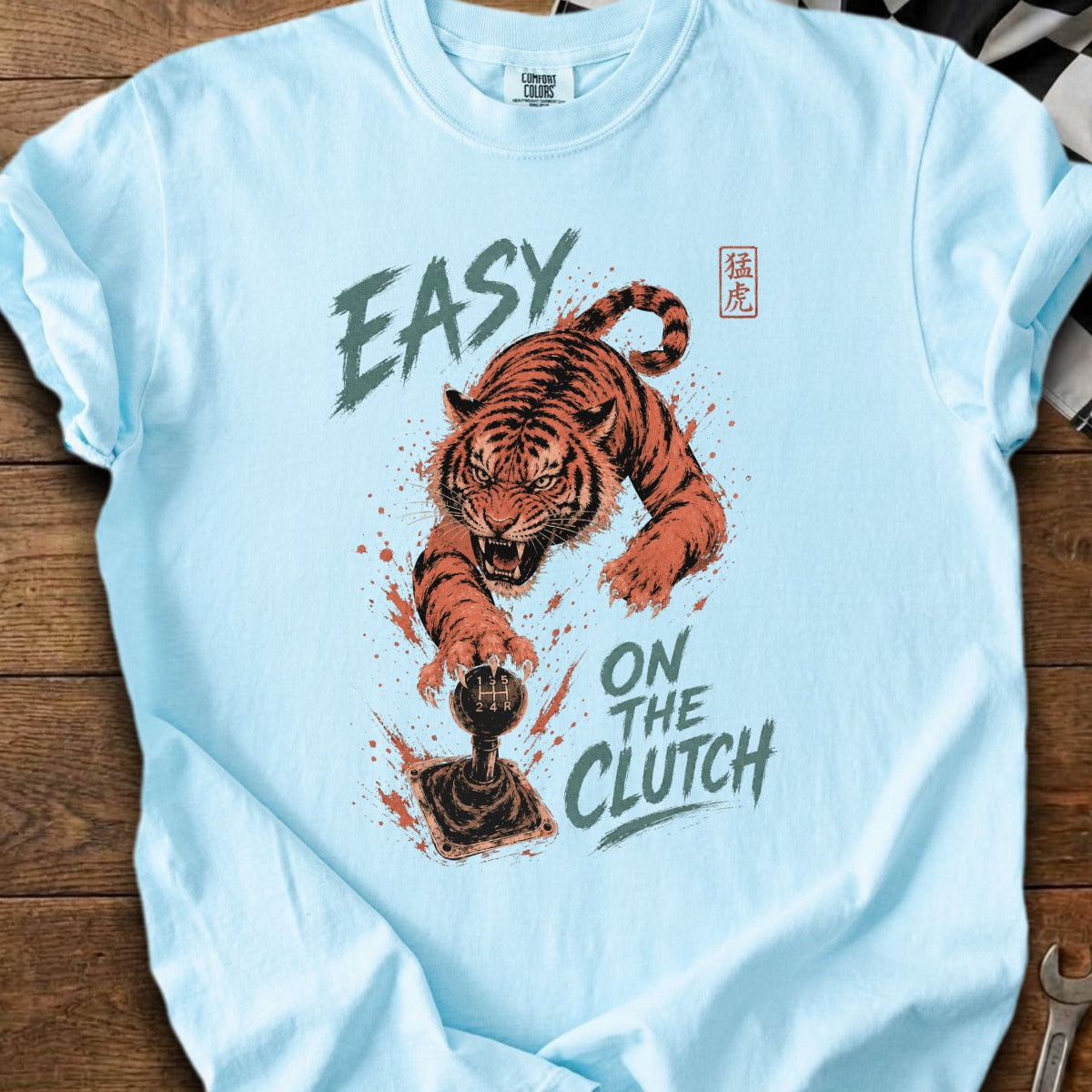 Light blue t-shirt with a tiger lunging at a manual transmission shift knob, text "EASY" and "ON THE CLUTCH".