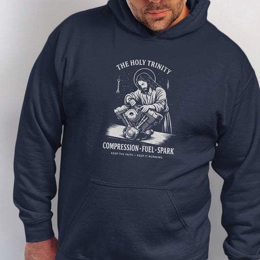 Jesus works on a motorcycle engine with text "The Holy Trinity" and "Compression Fuel Spark".