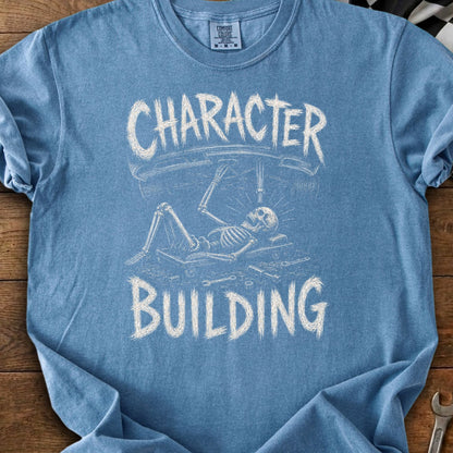 Blue t-shirt with "CHARACTER BUILDING" text and skeleton working under a car.