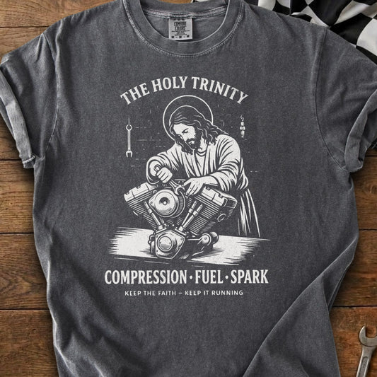 Jesus works on a motorcycle engine with text: The Holy Trinity, Compression Fuel Spark, Keep the Faith.