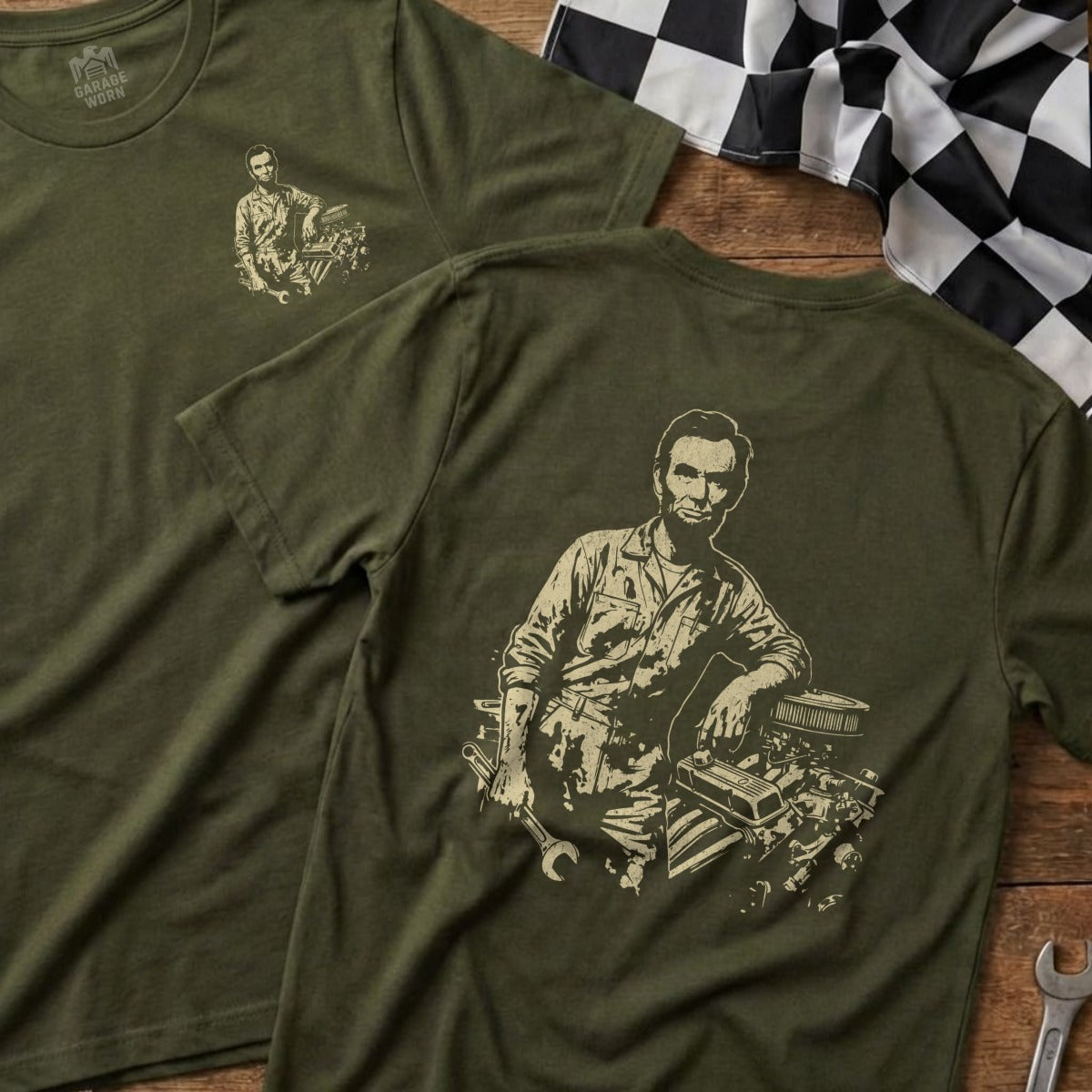 Abraham Lincoln leans on a car engine with tools on an olive green t-shirt.