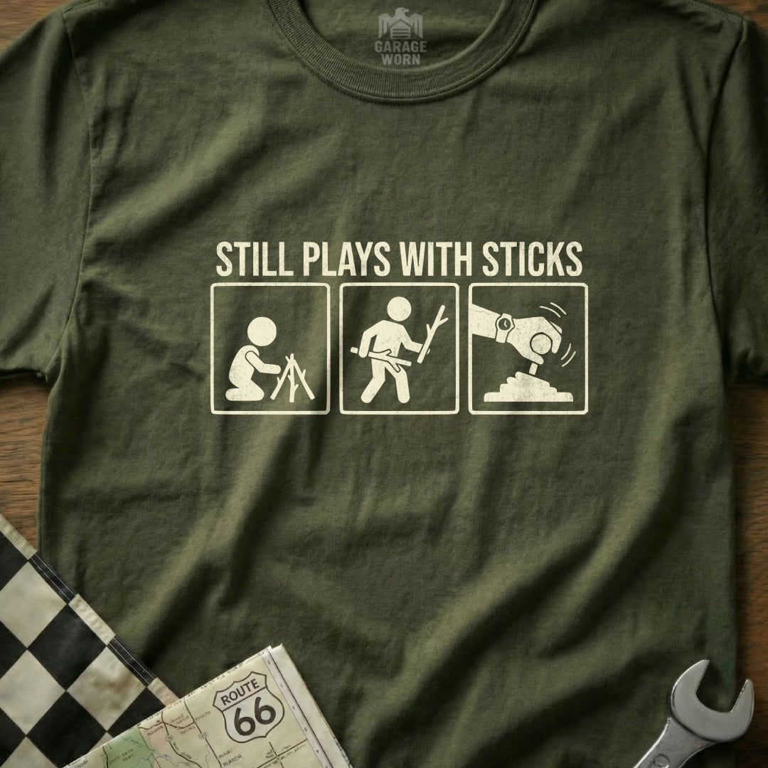 T-shirt with "Still Plays with Sticks" graphic depicting three stick figures.