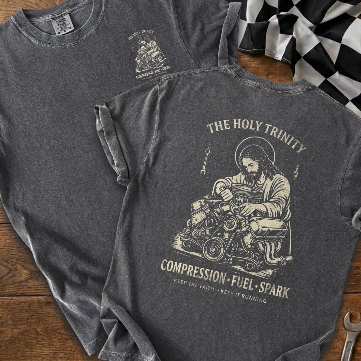 Dark grey t-shirt with Jesus working on an engine, reads "The Holy Trinity".