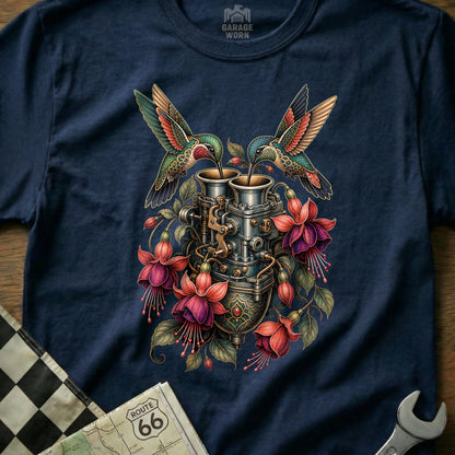 Two hummingbirds drink from a vintage carburetor surrounded by fuchsia flowers.