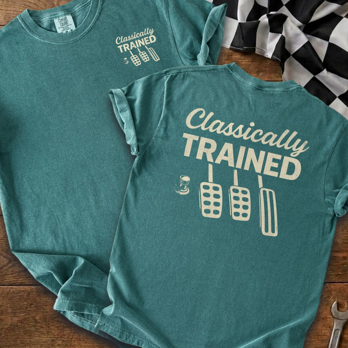 Teal t-shirt on wooden surface with "Classically TRAINED" and pedal graphics.