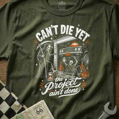 Grim Reaper watches a skeleton working on a car under the text "Can't Die Yet".