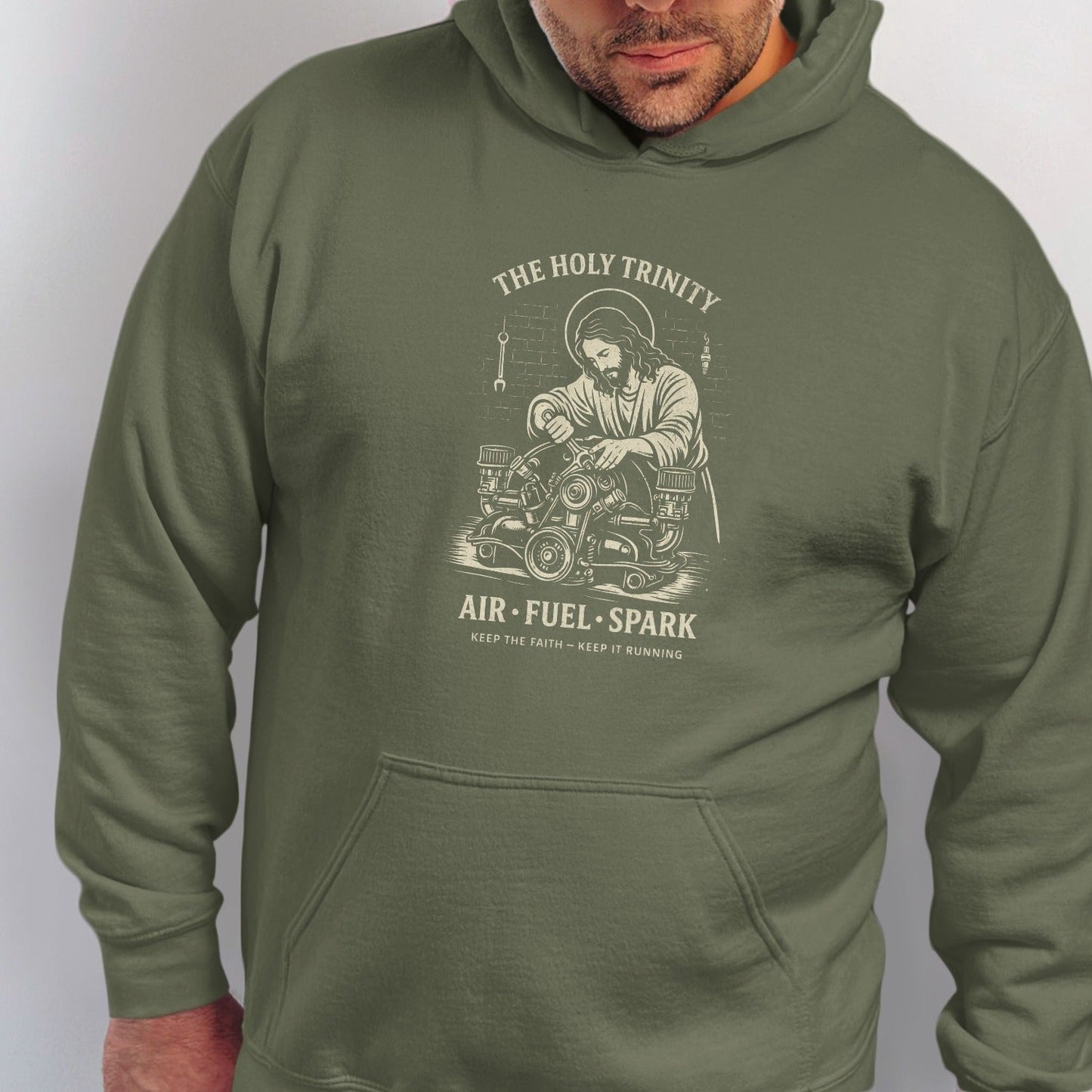 Green hoodie with white graphic of Jesus working on an engine. Text: "The Holy Trinity, Air Fuel Spark".