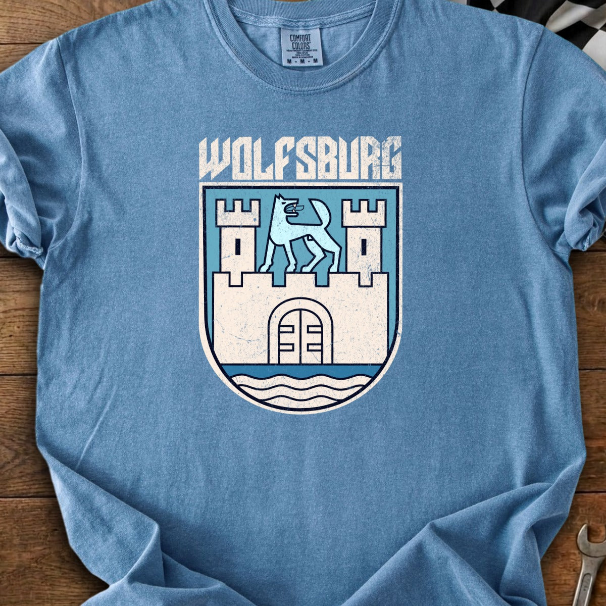 Blue t-shirt with a "Wolfsburg" coat of arms featuring a wolf and castle design.